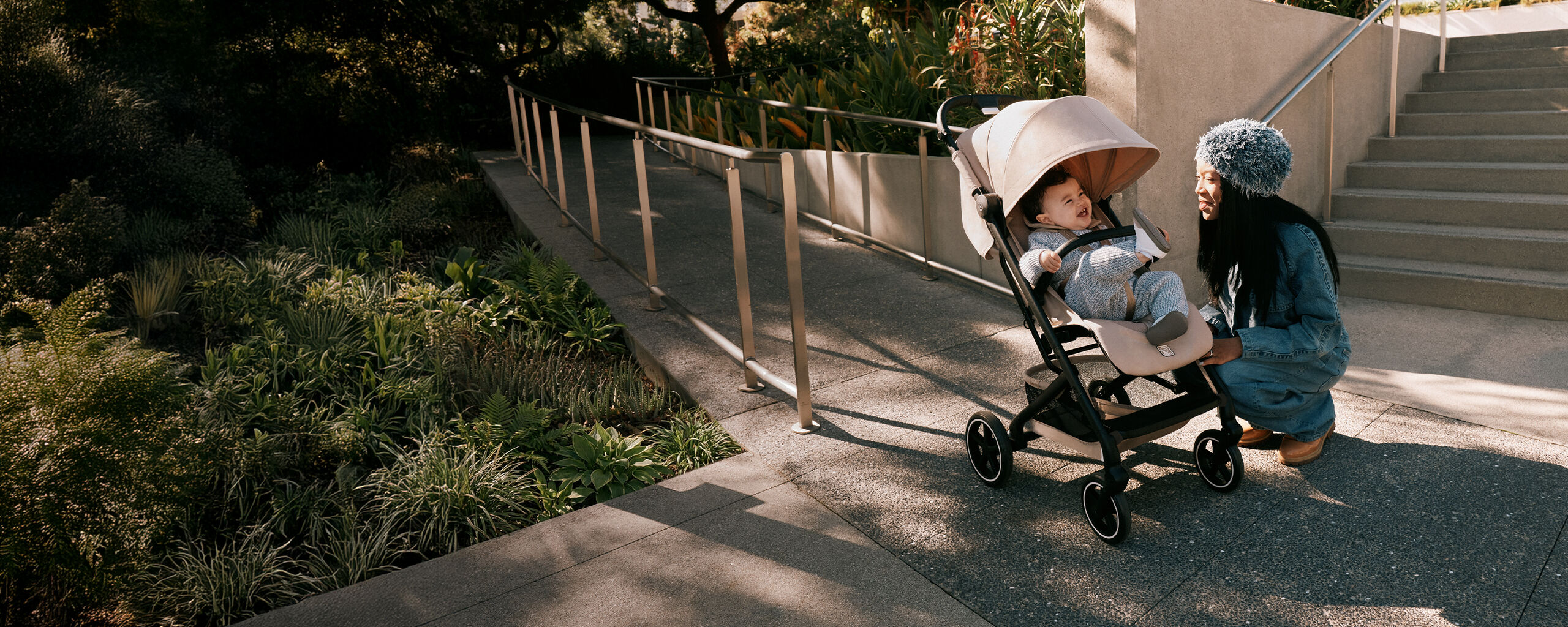 Une m&egrave;re &agrave; genoux pr&egrave;s de sa poussette compacte Beezy, son enfant riant &agrave; l&rsquo;int&eacute;rieur.