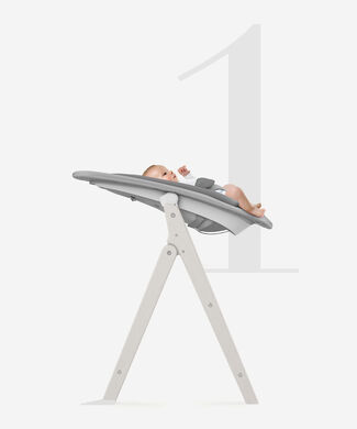 A baby is lying in a grey Click and Fold high chair, set in a reclined position.