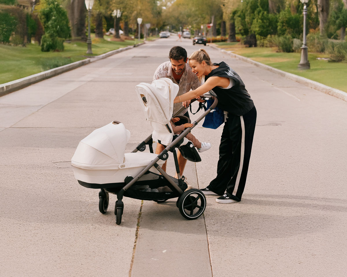 Man pushing a pram with a baby car seat against a yellow background.