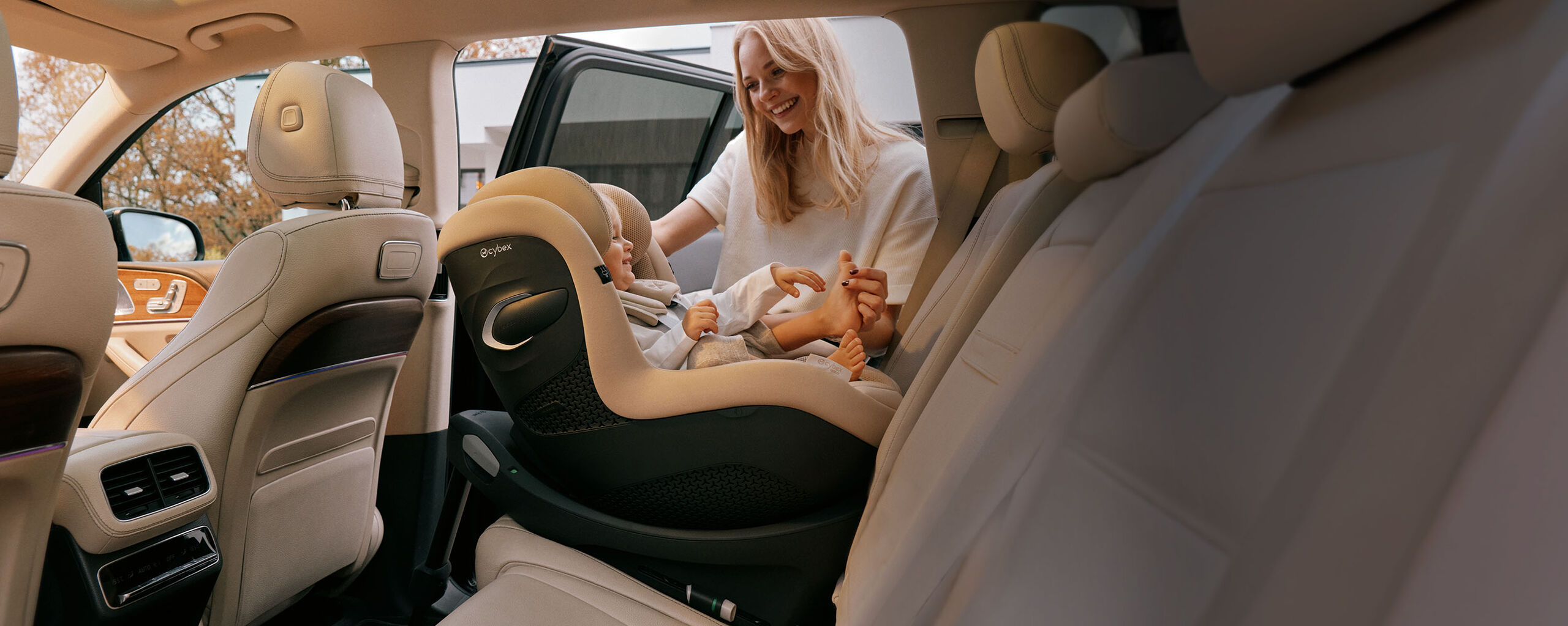 Woman smiling at her daughter while she tickles her foot. The daughter is sitting in a Sirona G i-Size car seat that is turned rear-facing. 