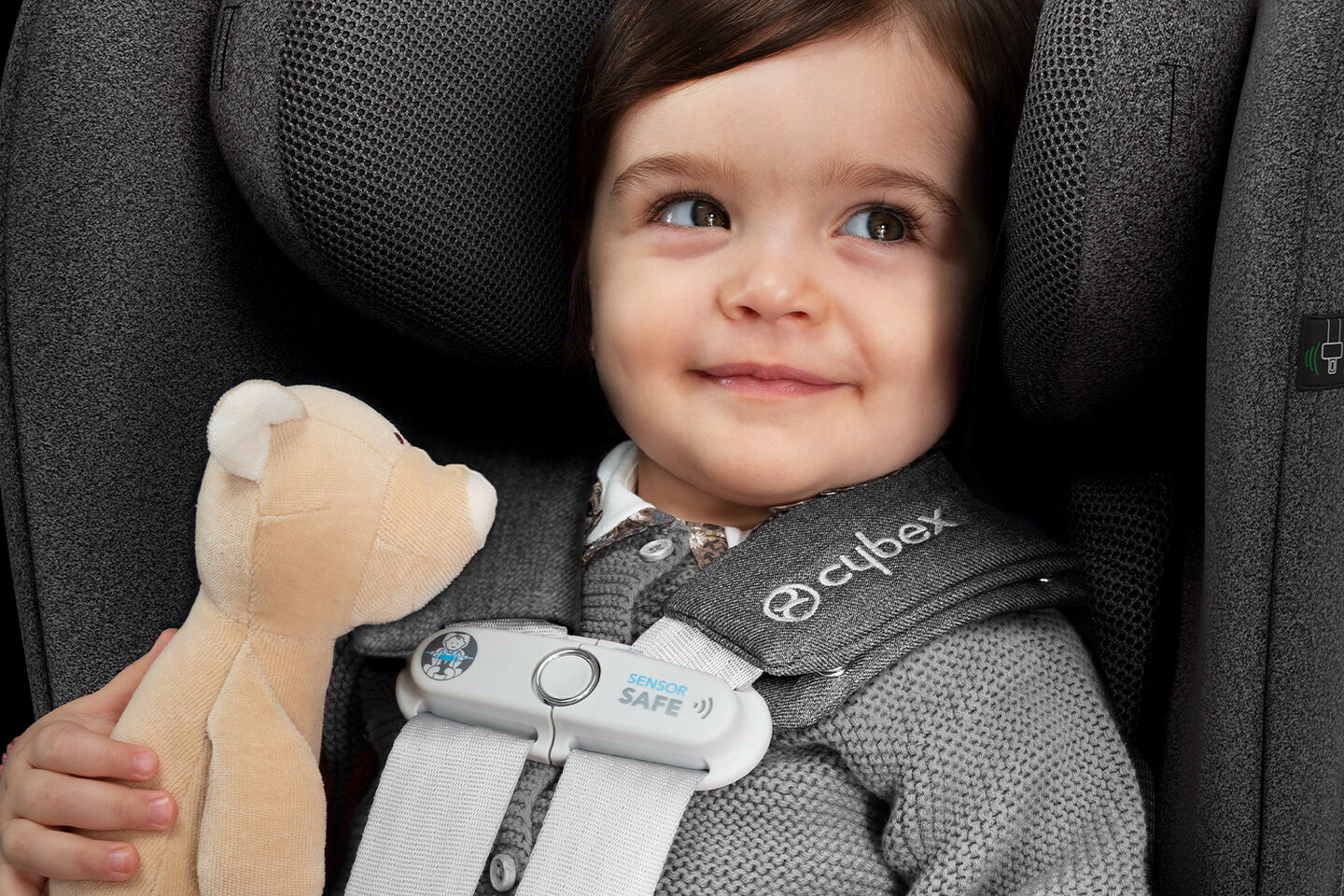 Enfant en bas &acirc;ge dans un si&egrave;ge auto Cybex tenant un animal en peluche.