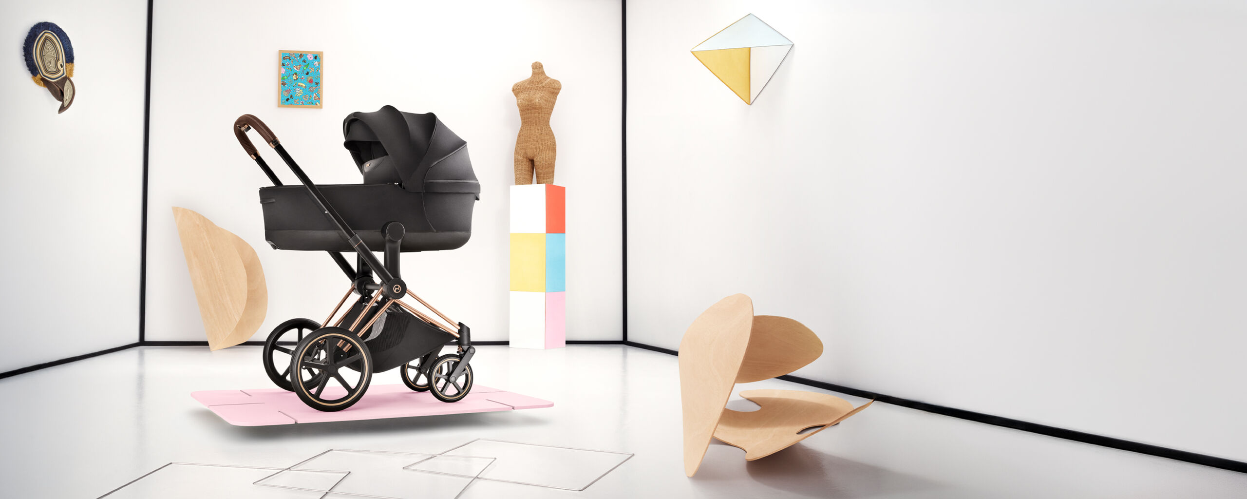 A Priam stroller on a pink thin platform. Various shapes and forms scattered behind and next to it.