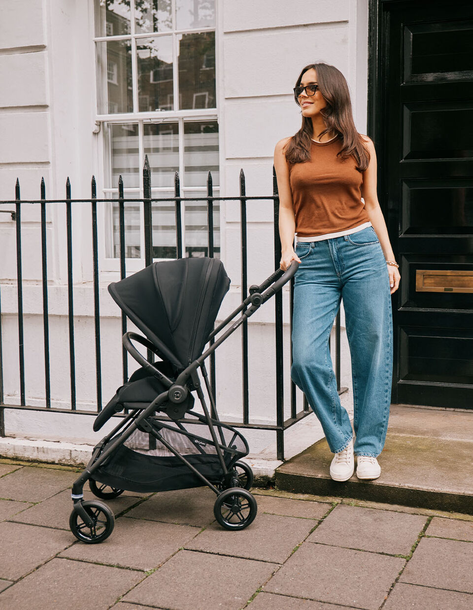 The lightweight pushchair Melio Carbon is positioned next to a stylish woman by a fence.