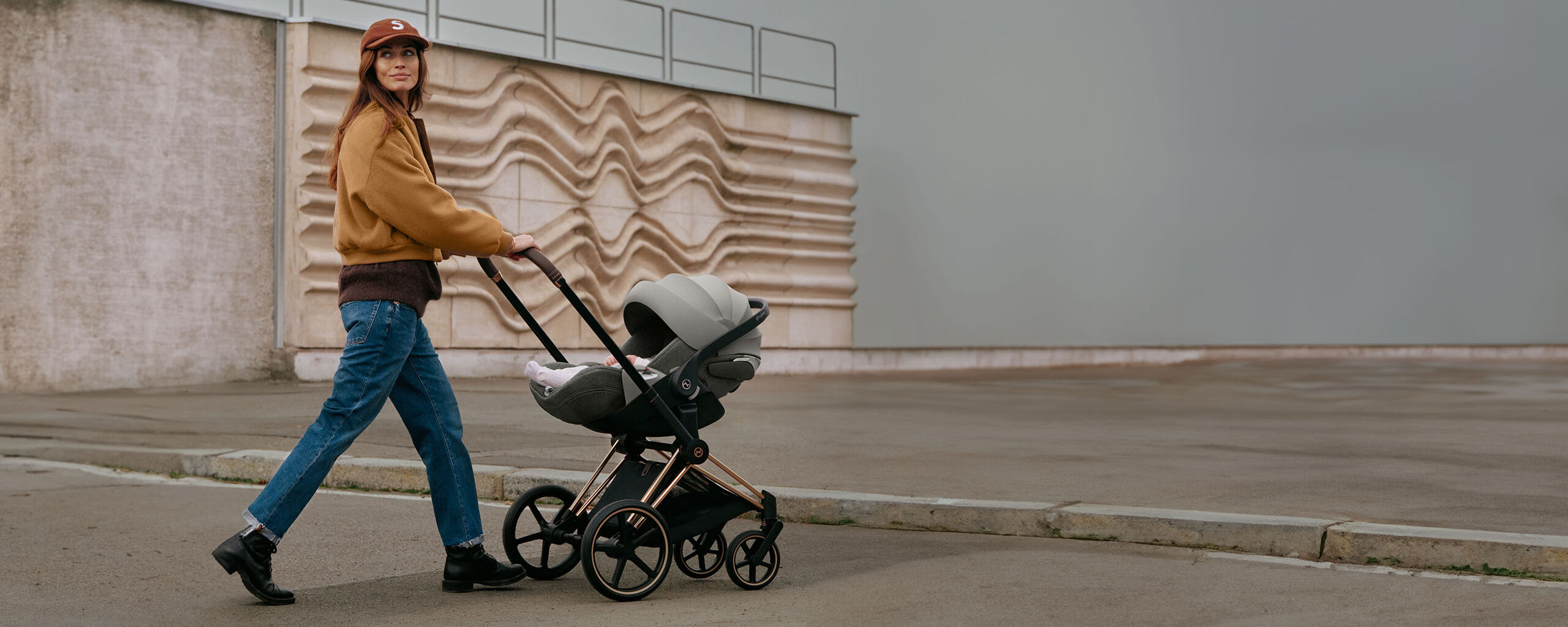 Woman pushing a pram with the Cloud T reclining infant car seat in front of a textured wall.