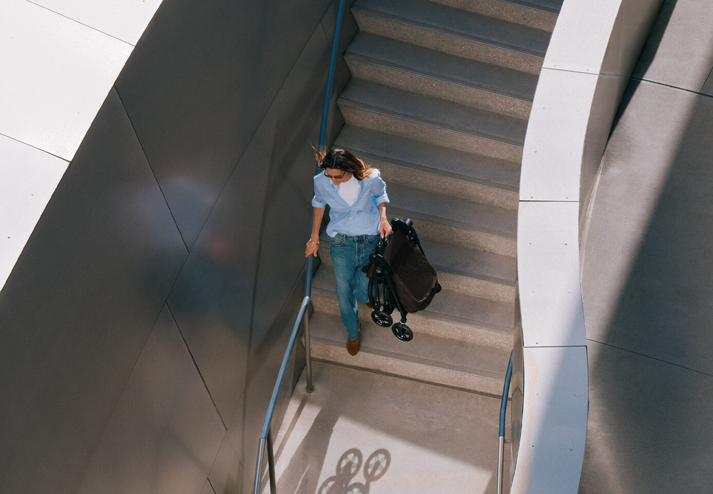 Una donna sale una scala trasportando il passeggino leggero Melio Carbon, con un cartello della metropolitana sullo sfondo.