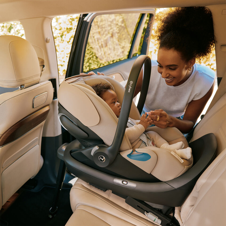 A smiling baby sits in a white car seat inside a vehicle.