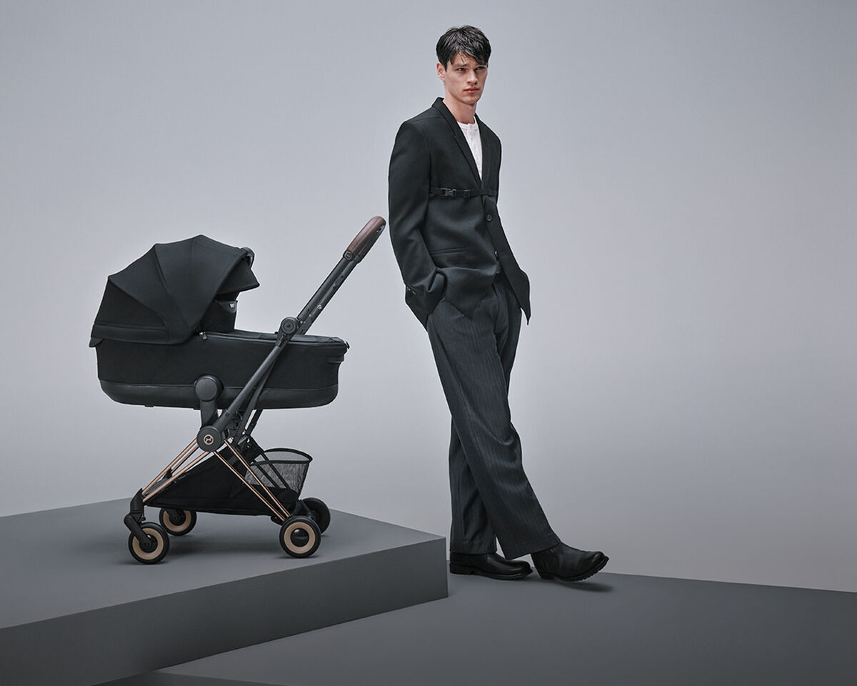 A man dressed in a suit next to a Coya lightweight stroller with a cot attached.