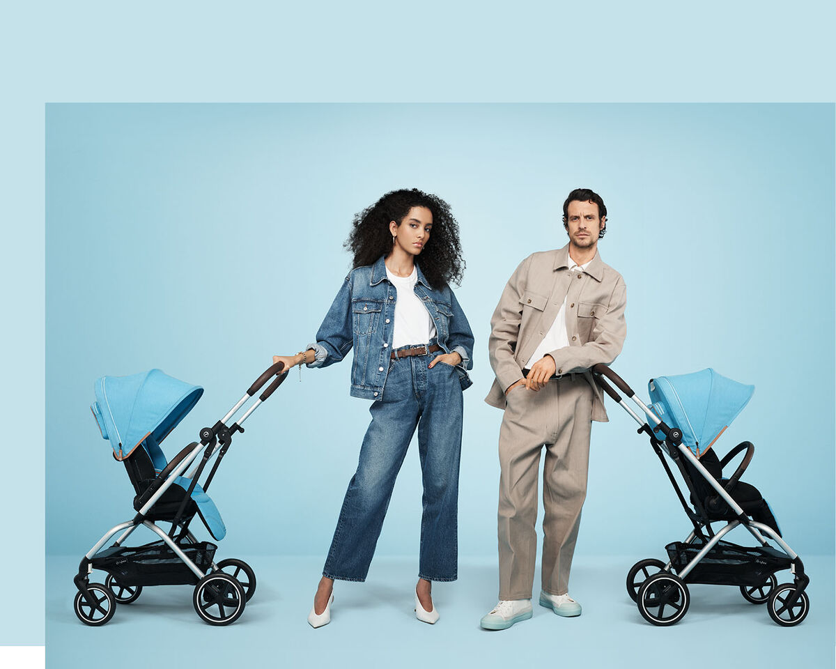 Two people posing next to two blue Eezy S Twist +2 pushchairs against a light blue background.