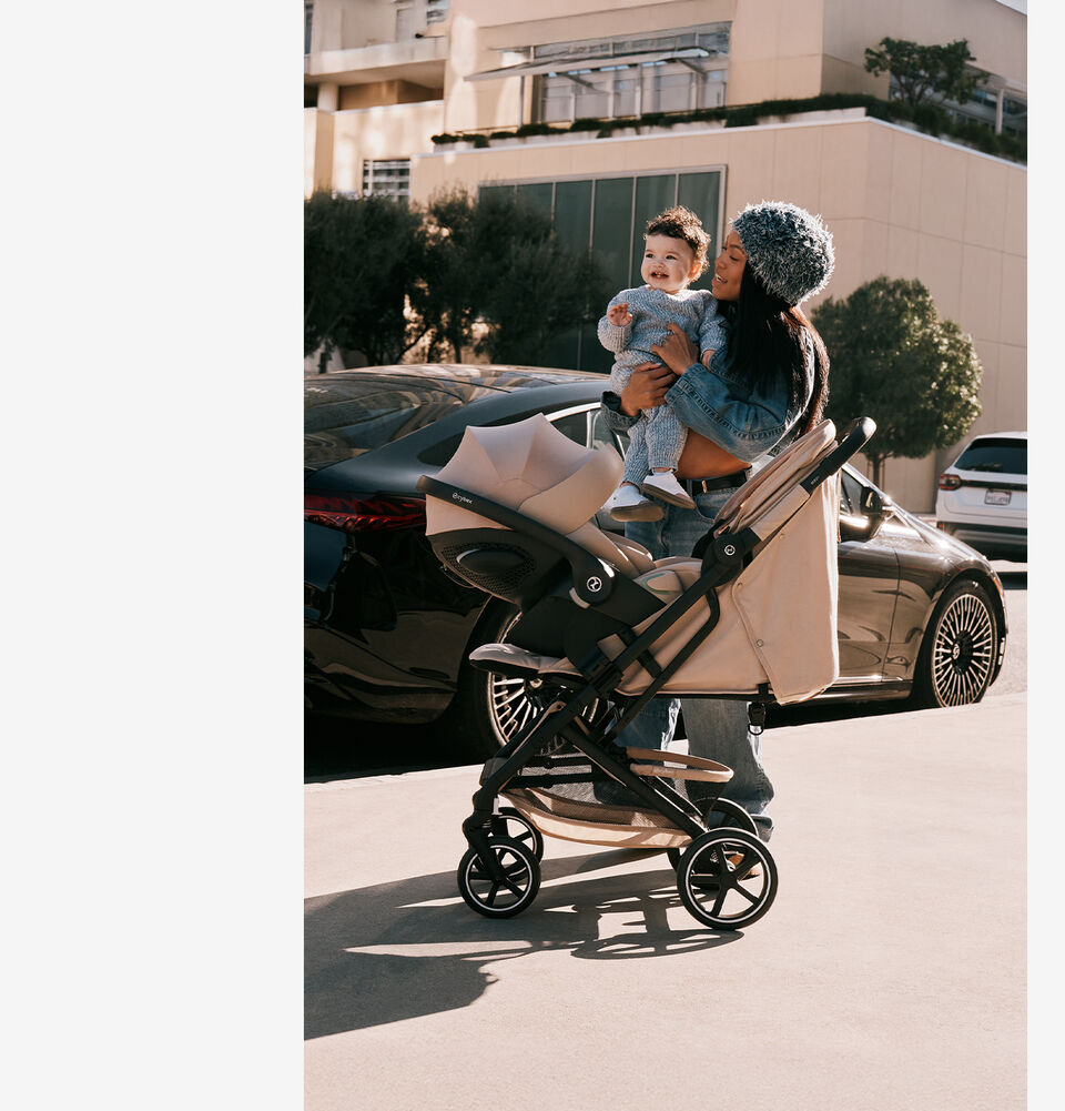 Une femme tenant son b&eacute;b&eacute; avec une poussette compacte Beezy &eacute;quip&eacute;e d&rsquo;une coque auto pour b&eacute;b&eacute;.