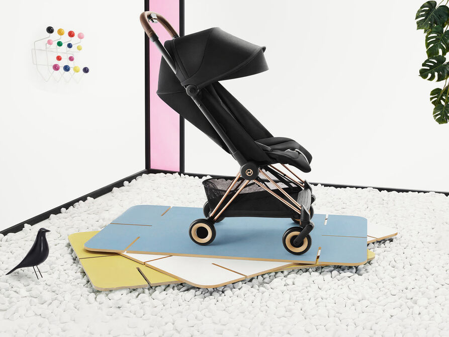 Black stroller with canopy on colourful mats, surrounded by white stones and decor.