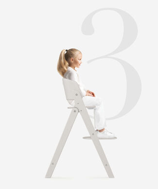 A young girl sitting on a white Click and Fold high chair against a large grey background with the number three.