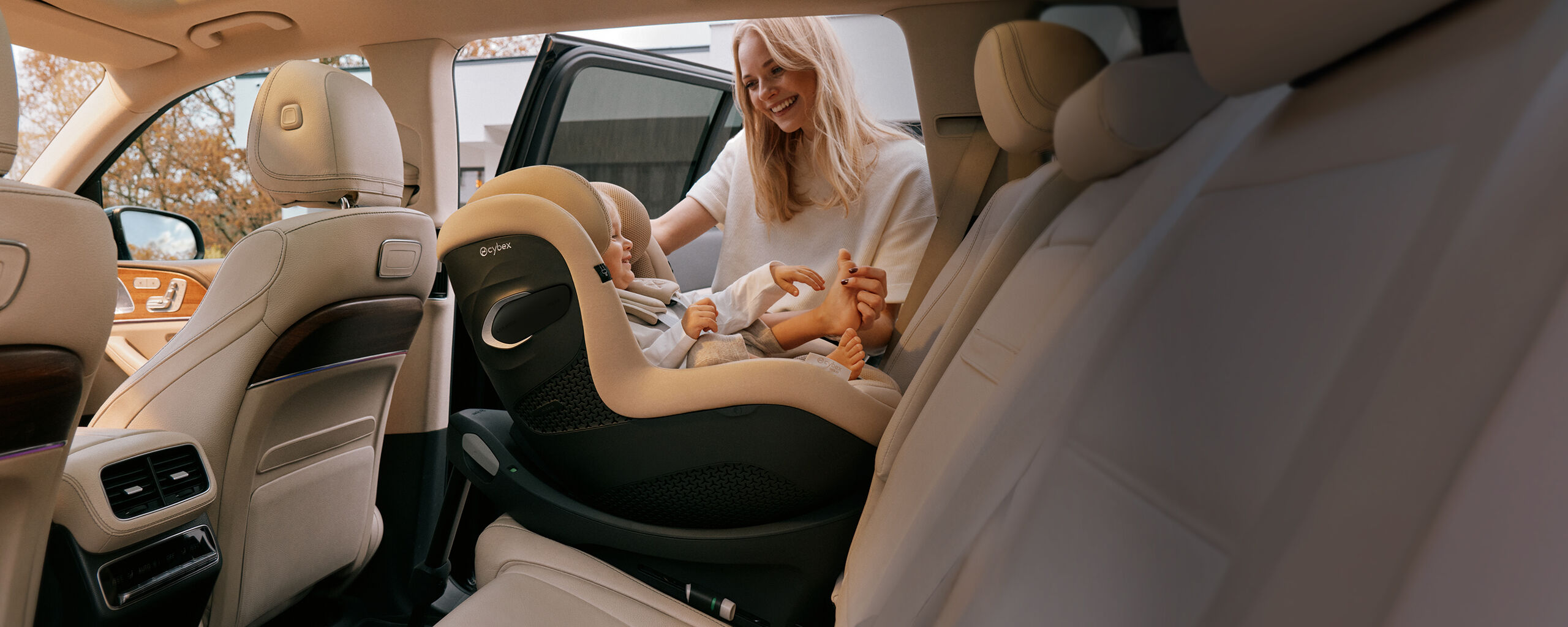 Woman smiling at her daughter while she tickles her foot. The daughter is sitting in a Sirona G3 car seat that is turned rear-facing. 